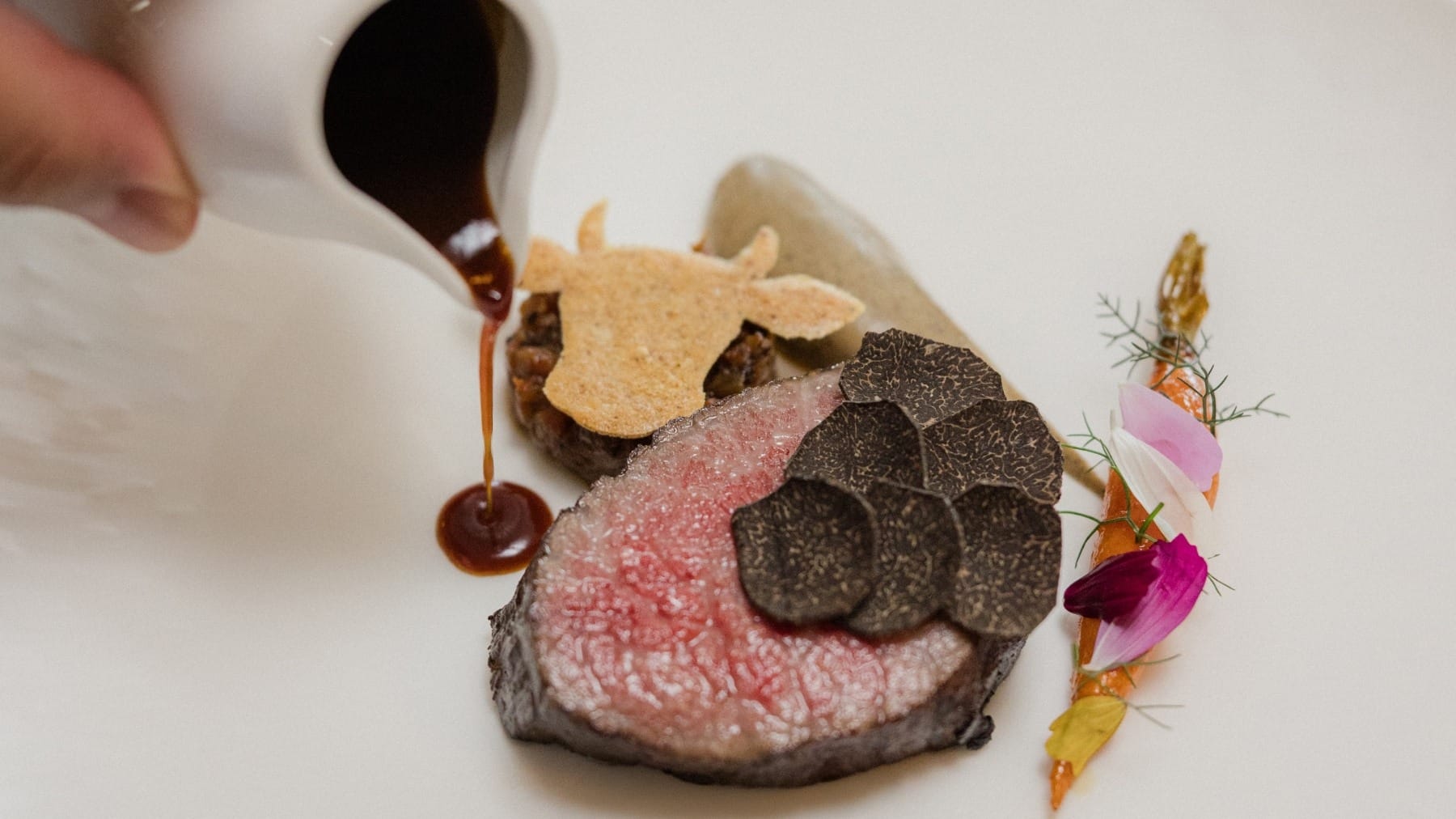Grilled A5 wagyu tenderloin with roasted celeriac, fricandó purée, black pepper sauce, baby carrot, moixernó cracker, and shaved black truffle.